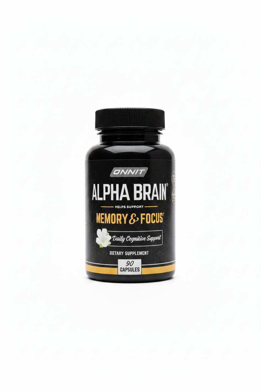 A hand holding a black bottle of Unnit Alpha Brain Memory & Focus dietary supplement capsules, with a desk and books in the background.